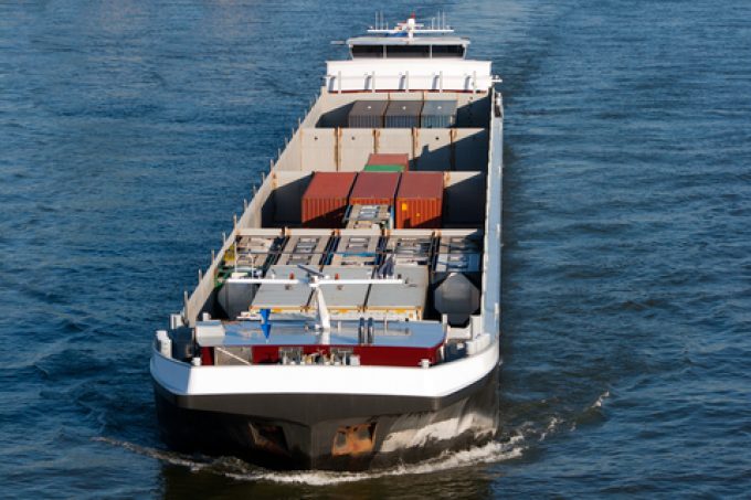 A heavily laden barge navigating a shallow section of the Rhine River with dry, exposed riverbanks visible.