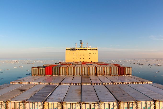 A container ship navigating through icy Arctic waters with a South Korean flag visible.