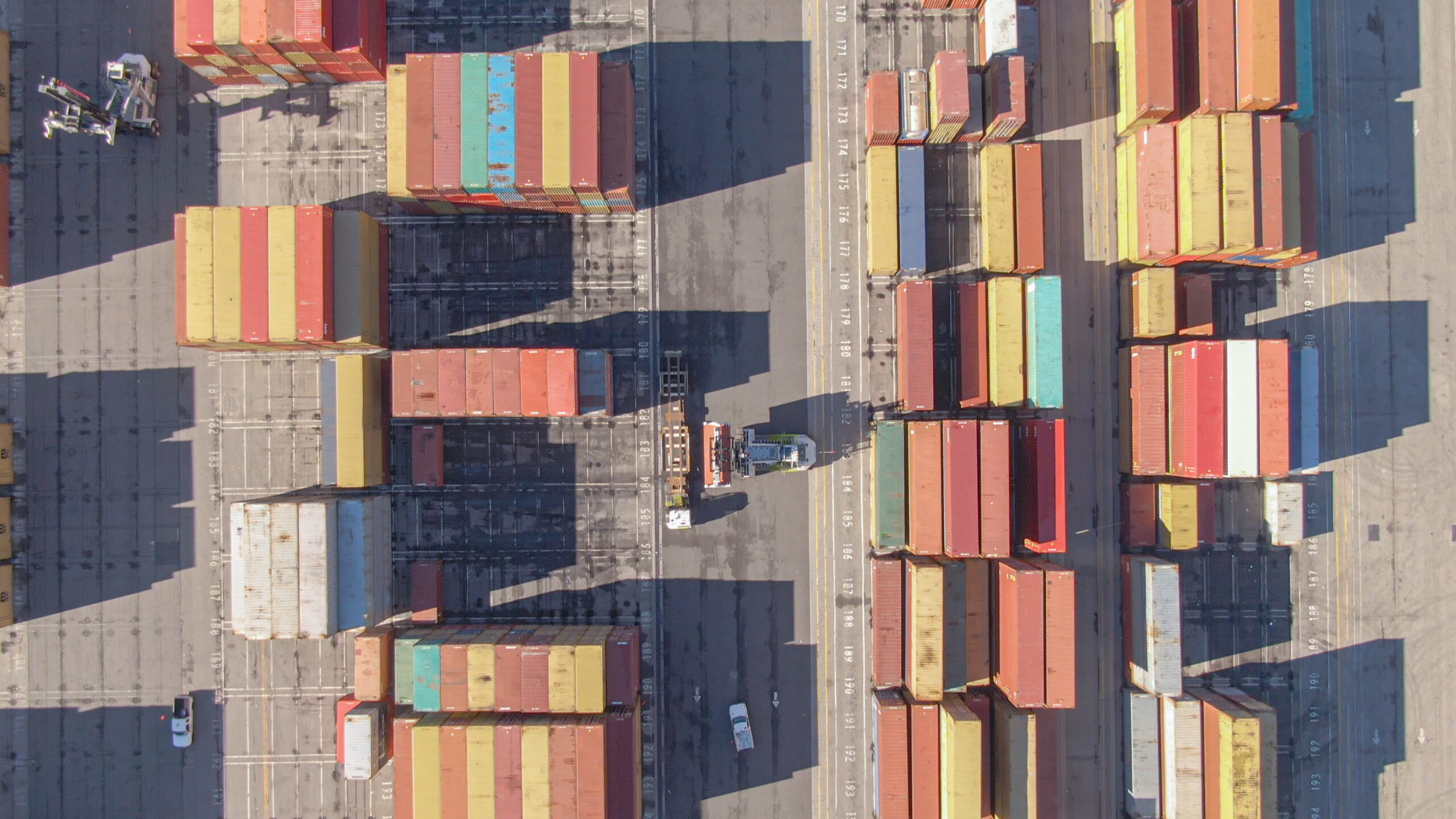 Containers stacked at Port of Los Angeles terminals under cloudy skies, with cranes active amid March operations