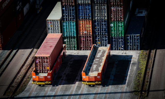 A stylized image of a magnifying glass hovering over shipping containers, symbolizing detailed investigation into logistics.