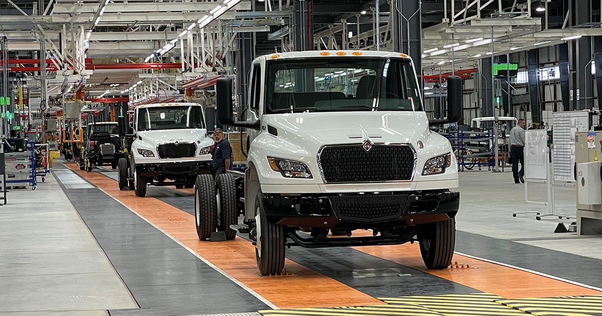 A row of parked medium-duty trucks on a lot, some showing signs of age.