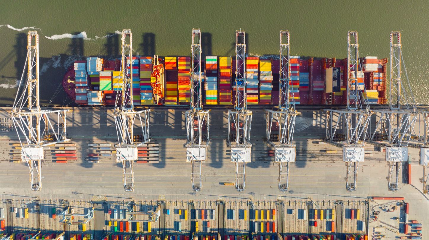 A large cargo ship docked at a port with cranes and containers visible.
